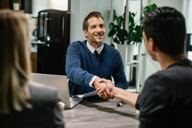 Happy financial consultant greeting his clients while meeting them at their home.  Me are shaking hands.